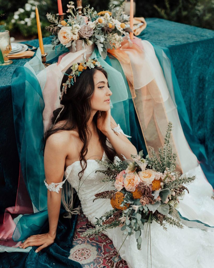 Girl lounges in front of the lavish head table wearing a flower crown and beautiful wedding dress for the styled shoot of VendorPalooza.