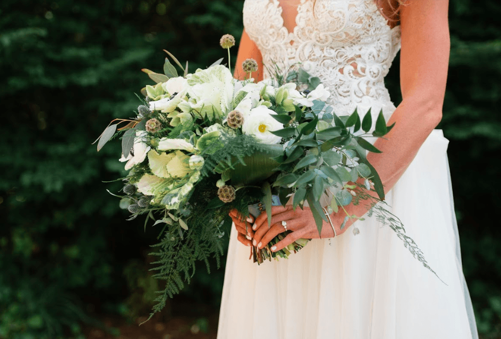 An up close shot that shows the bridal bouquet, engagement ring and lace detail on a wedding dress from All About the Bride.