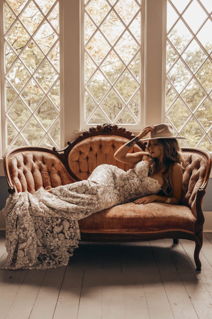 Boho glam bride poses on a couch before her wedding