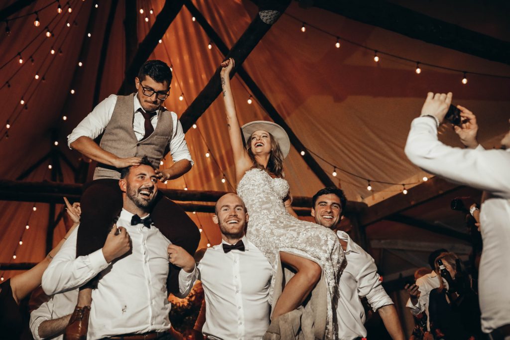 Bride and groom dance on the shoulders of their bridal party at their boho glam wedding.