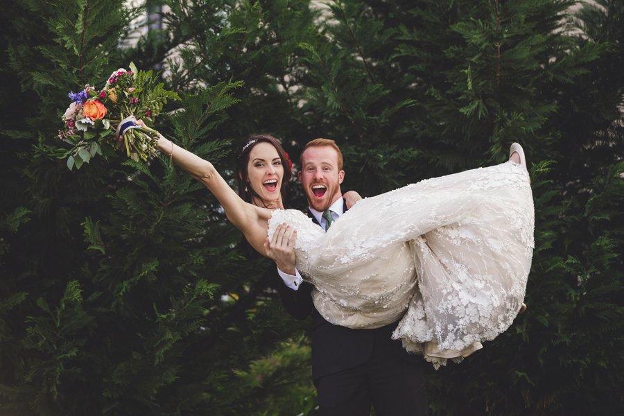 Groom cradles bride up in the air to show off their excitement about getting married in this authentic photo.